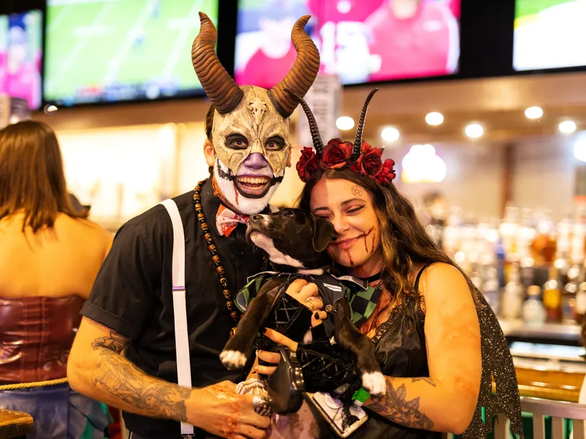 Couple in horned costumes with their costumed puppy at a Halloween bar crawl